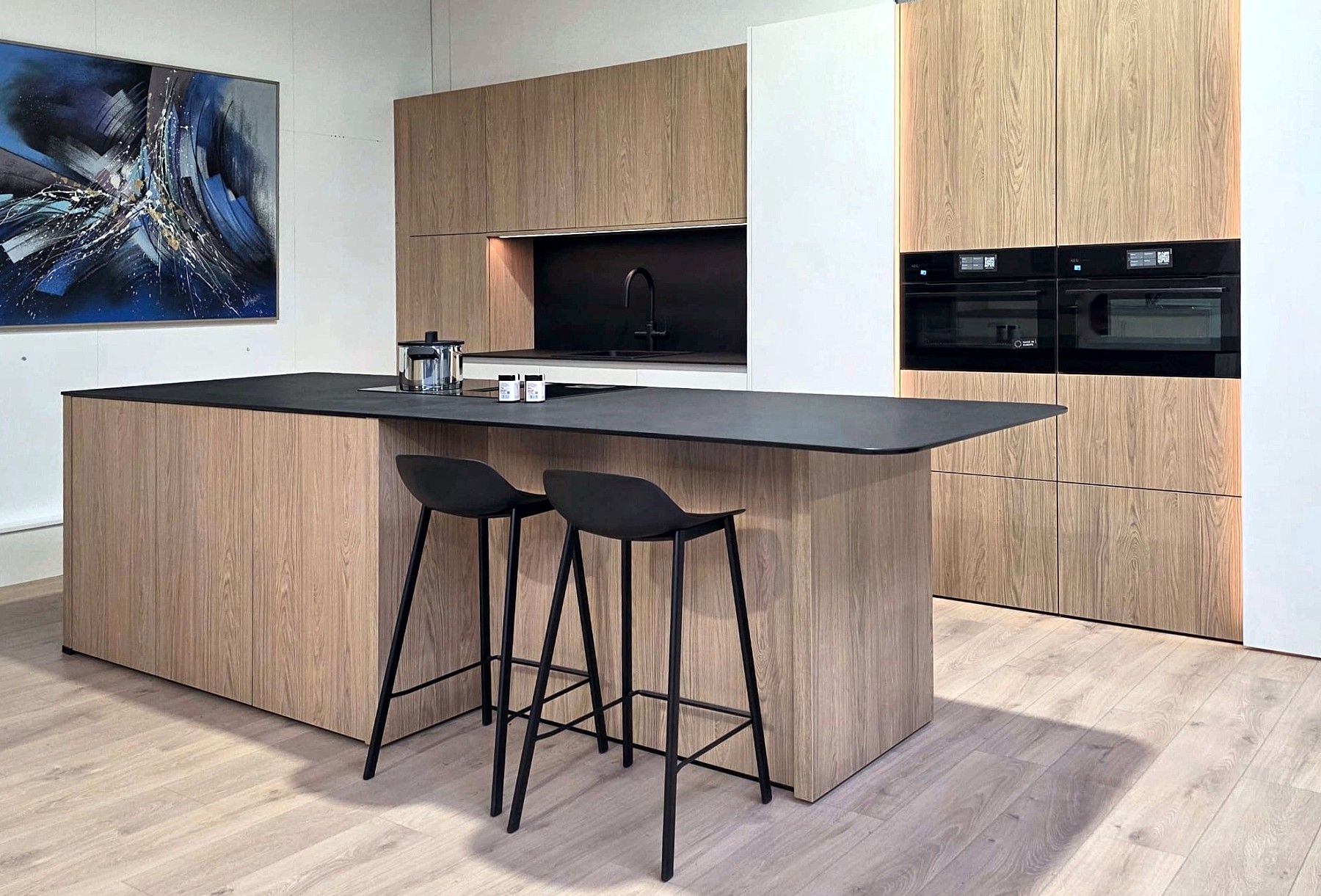 Keuken in eik met een zwart werkblad: een eiland met twee barkrukken voor een kastenwand met ingebouwde ovens